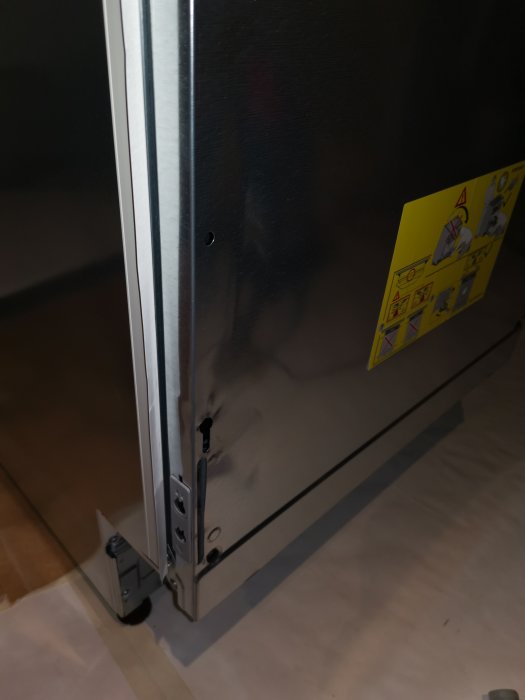 Närbild på en bucklig diskmaskin med fästningsdetaljer synliga och en varningsetikett.