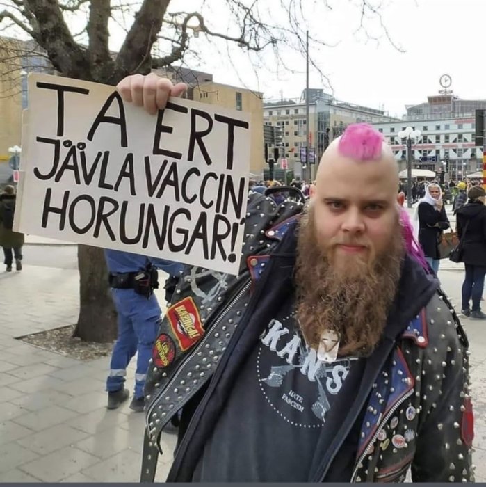 Person med rosa mohawk och skinnjacka håller upp skylt med budskap om vaccination.