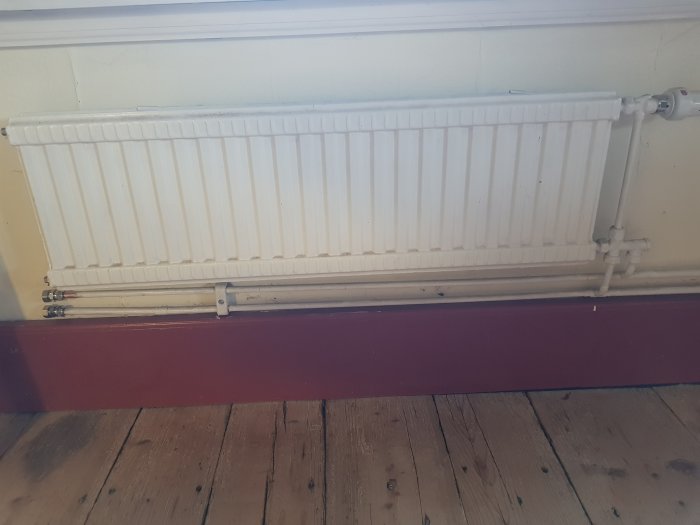 En radiator med pluggad matning och returledning på väggen i ett renoverat rum.