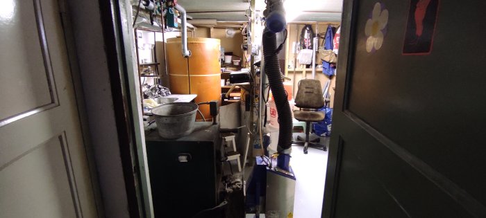 Trångt pannrum med gammal ackumulatortank och varmvattenberedare, omringat av diverse föremål.