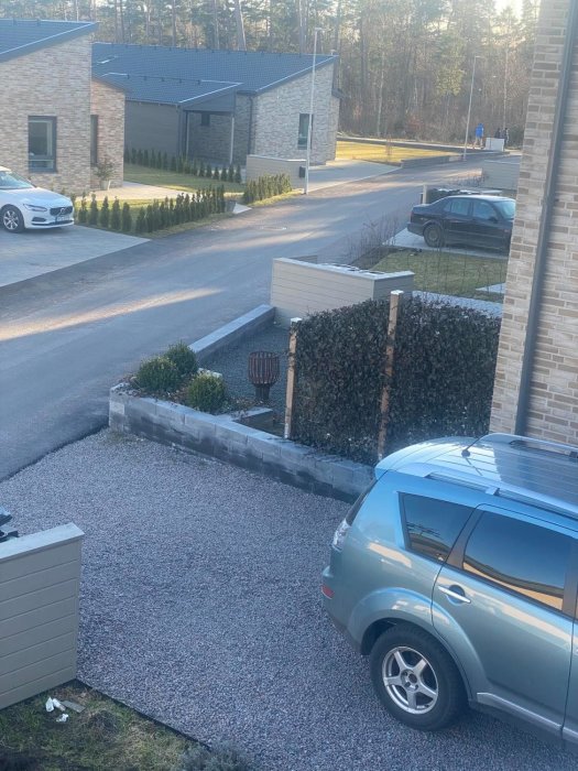 Vy över en uppfart med grus och en låg stenmur som omger en höjd rabatt vid sidan av huset.