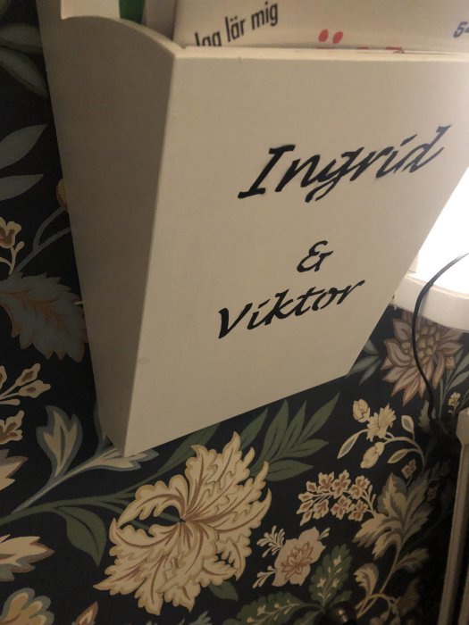 Ett postfack målat med namnen "Ingrid & Viktor" i svart airbrushad stil mot en blommig bakgrund.