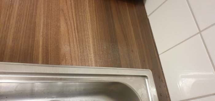 Laminatbänk med vita fläckar nära en diskho, med möjlig skada från rengöringsmedel eller kalk.