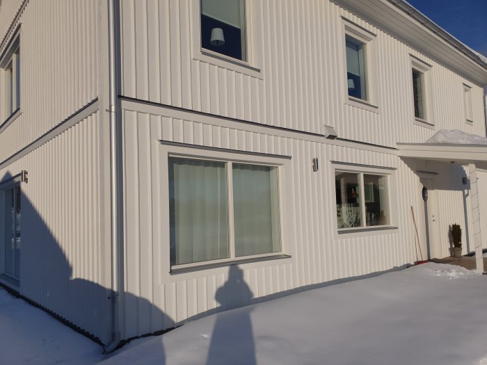 Tvåvåningshus i vitt med plåtdetaljer ovanför fönstren och snötäckt mark.