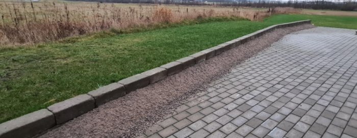Stenlagd gångväg med kantsten och grus vid kanten, grön gräsmatta i bakgrunden.