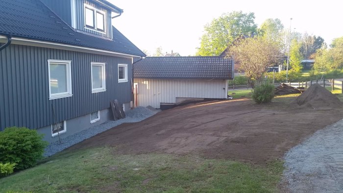 Ett nyplanerat gräsmarksområde vid ett hus med en hög jord och en grusgång på sidan.