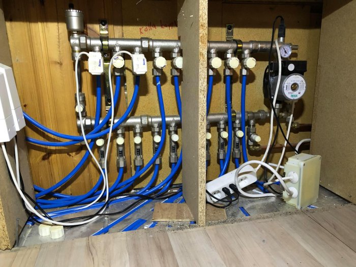 Värmesystemsinstallation med kopplingar, rör och cirkulationspump under trappa.