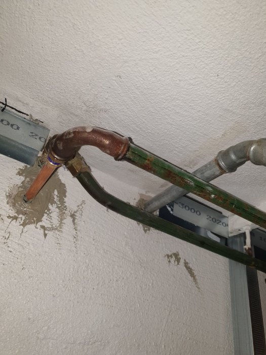 Gamla rör i en källare, synliga tecken på äldre installationer och en tång fäst vid ett av rören.