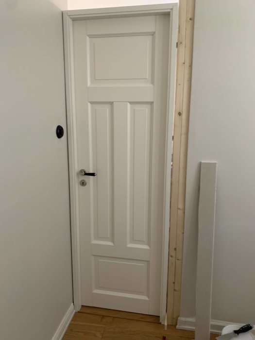 En vit dörr monterad nära väggen med omålade dörrfoder till vänster.
