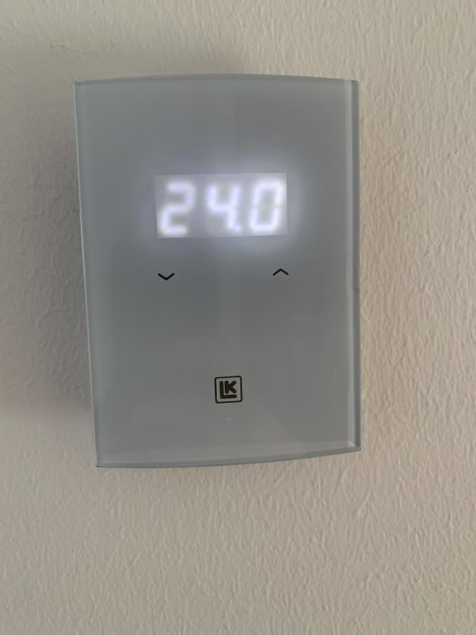Termostat med digital display som visar "240" på en vit vägg, symbol för ett märke synligt.