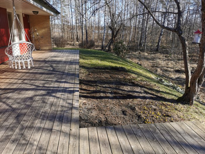 Altan vid hus med hängstol, gräsmatta och skog i bakgrunden, utbyggnad planeras.