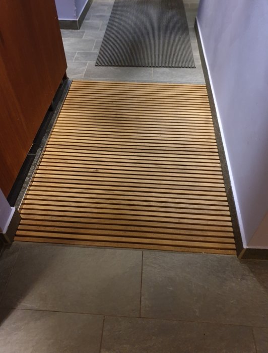 Träribbor som ligger jäms med kakelgolv vid en golvbrunn i badrum, planerat för vattenavrinning.