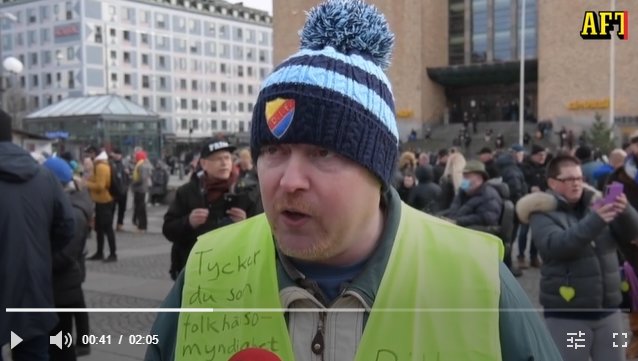 Man i mössa och väst talar, folkmassa i bakgrunden på Medborgarplatsen.