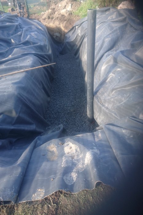 Pågående dräneringsarbete med grusgång och svart dräneringsrör omringade av geotextil.