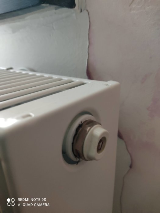 Termostat på radiator med nedsatt termostatknapp nära vitmålad vägg.