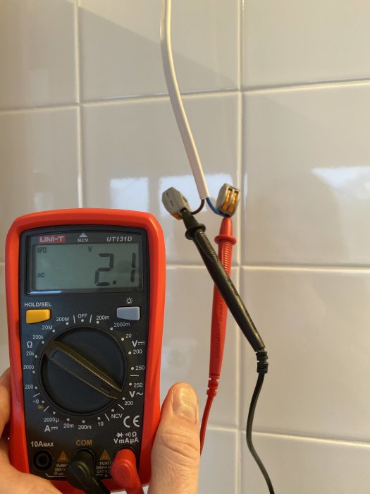 Multimeter som visar 2.1V mätt på två inkommande kablar mot kakelvägg.