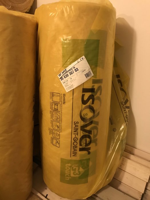 Isover glasullsisolering rullar staplade mot en vägg.