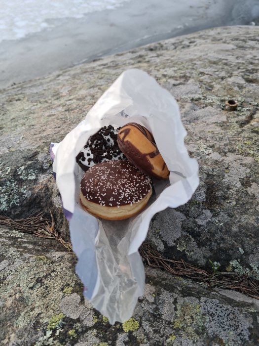 Chokladöverdragna munkar på ett papper på en stenig yta utomhus.