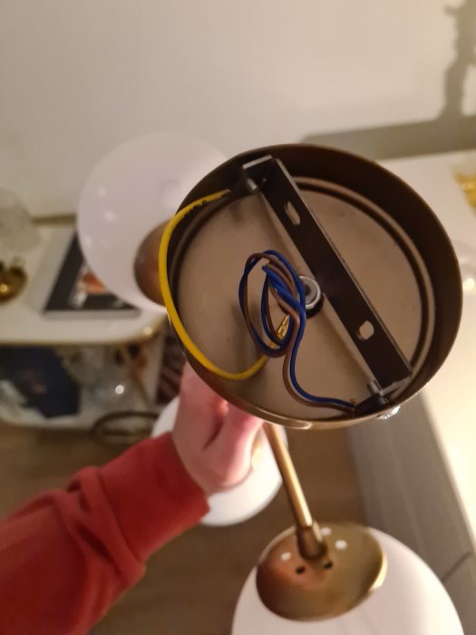 Hand håller en taklampskåpa upp och ner med synliga elledningar inuti, mot en otydlig bakgrund.