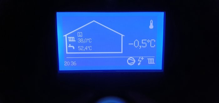 Digital termostat visar inomhus- och utomhustemperatur med husikon och varningsymbol.