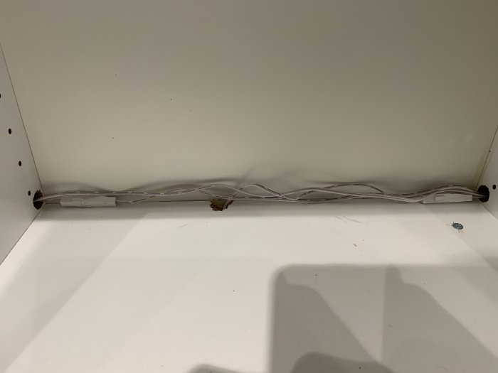 Nedslitna kablar löper längs baksidan av ett vitt köksskåp med synliga skador och hål i skåpets väggar.