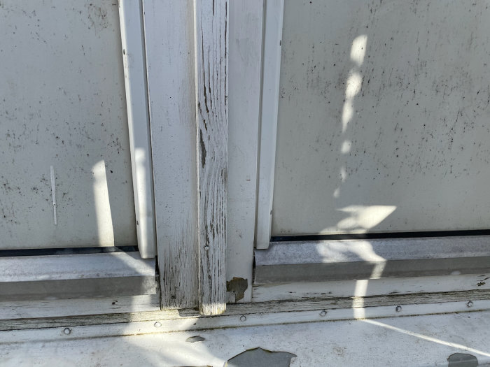 Äldre fönster med flagnande vit färg och synlig trästruktur på nedre delen av karmen.