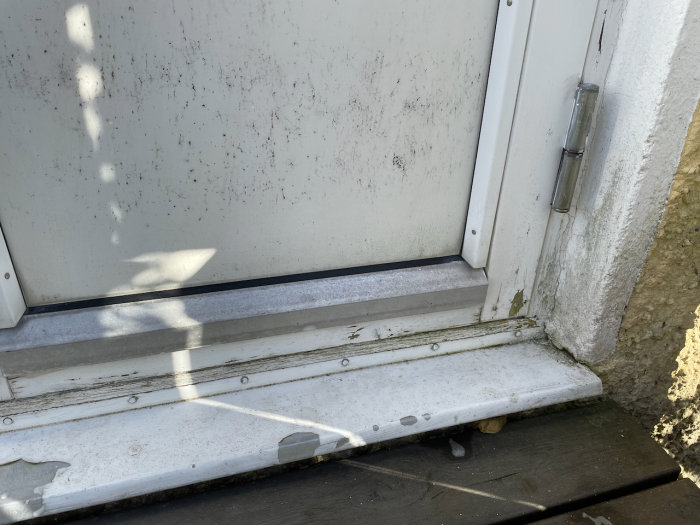 Gamla vitmålade fönsterkarmar med skadad och flagnande färg längst ned där det behöver renoveras.