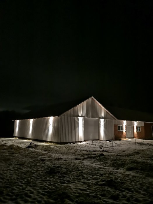 Ett belyst enfamiljshus på kvällen med snö på marken.