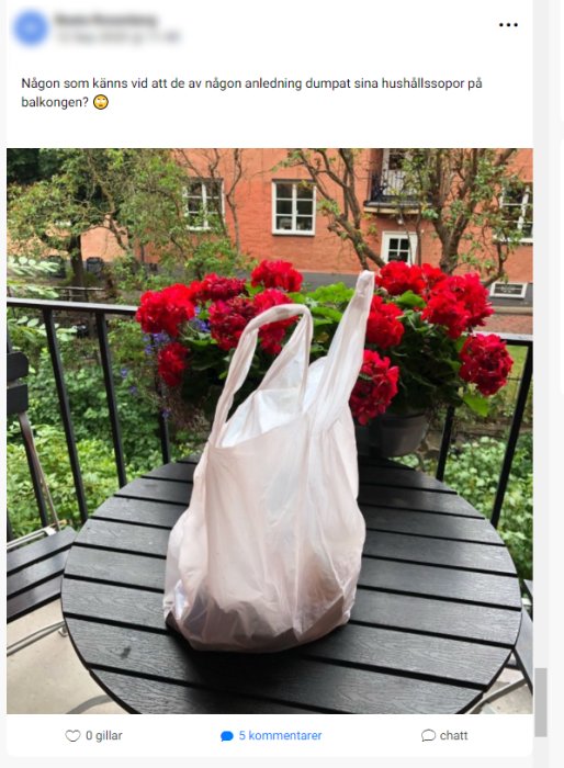 Plastpåse med hushållssopor på ett svart rund bord på balkong med röda pelargoner i bakgrunden.