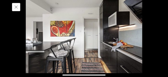 Modernt kök med svarta IKEA Voxtorp-luckor, barhäng med pallar och dekorativt konstverk på väggen.