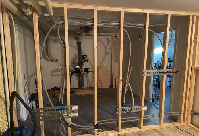 Badrum under konstruktion med synliga rörledningar och trästommar innan gipsskivor monteras.