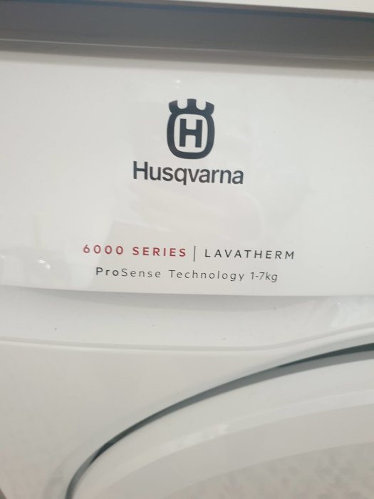 Närbild av en vit Husqvarna 6000 Series Lavatherm torktumlare med ProSense Technology 1-7kg etikett.