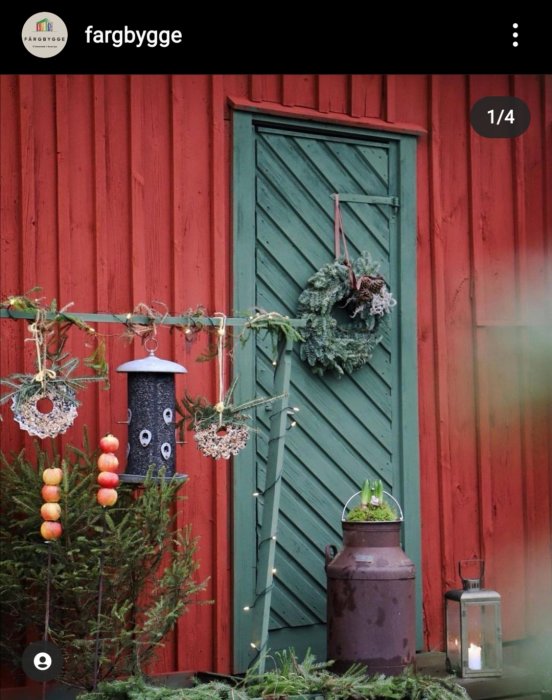 Rödmålad stuga med grönt dörrparti med krans, fågelhus och dekorationer.