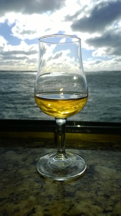 Ett whiskyglas fyllt med gyllene dryck mot en bakgrund av hav och moln.