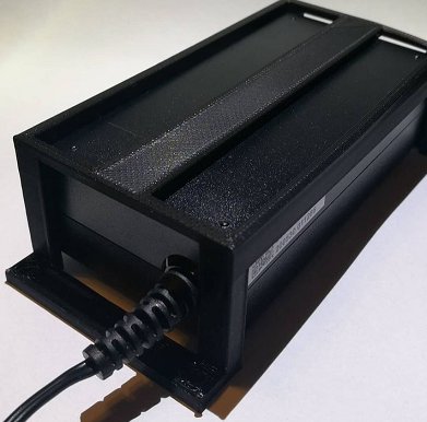 3D-utskriven hållare för strömförsörjning monterad under skrivbord med insatt kabel.