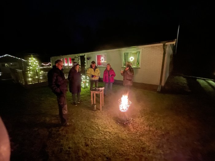 Personer samlade kring en brinnande cortenstål korglykta på en kvällsträff utomhus.