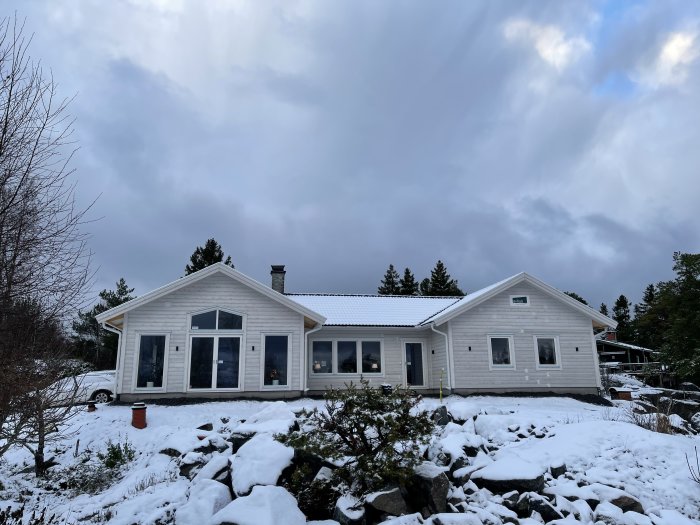Nybyggt enplanshus Villa Styrsö i vinterskrud med vit fasad och snötäckt trädgård i Norrtälje.