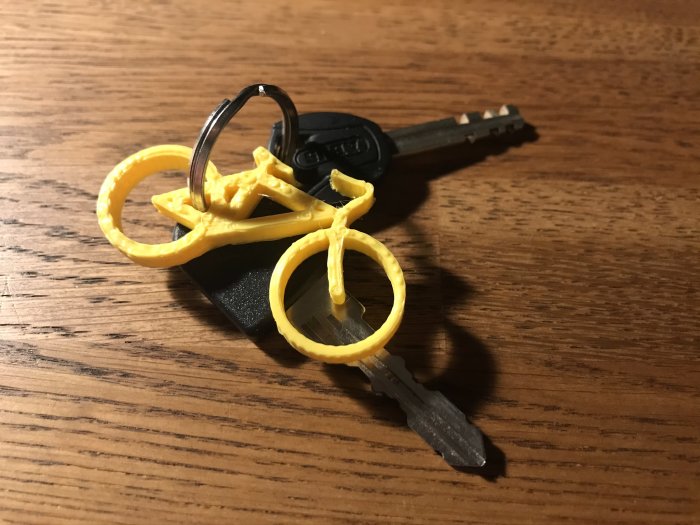 3D-utskrivna gula nyckelringar i plast fästa vid nycklar på ett träbord.