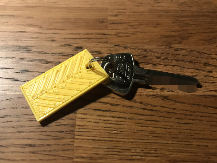 En 3D-utskriven gul nyckelring fäst på en metallnyckel, ligger på ett brunt träbord.