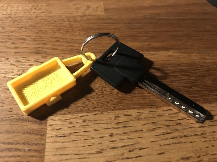 3D-utskriven gul nyckelring i plast bredvid en bilnyckel på ett träbord