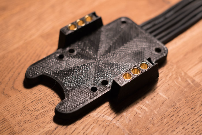 3D-utskrivet dammskydd i svart plast med inbäddade metallförstärkningar på ett träbord.