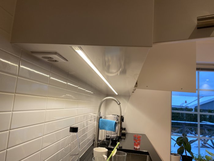 Kök med LED-list monterad under överskåp, dold kabeldragning och vita kakelväggar.