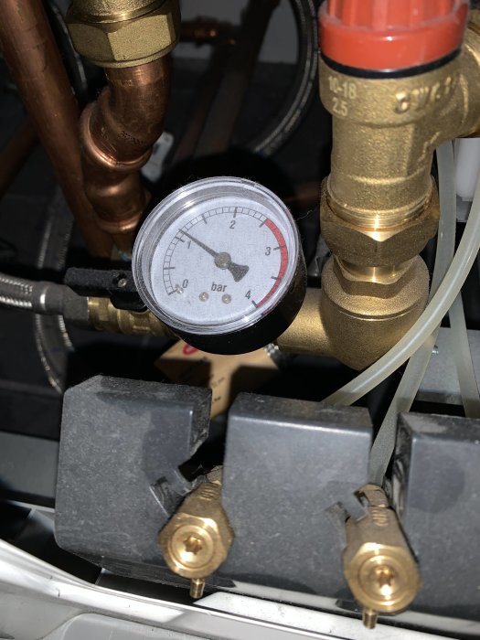 Manometer som visar trycket i en värmepump eller radiator med kopparledningar och justerventiler.