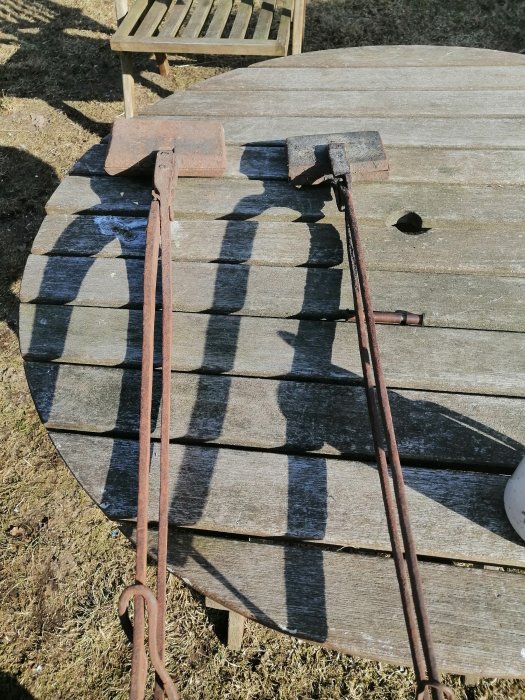Rostiga smidesverktyg på ett träbord utomhus, inkluderar en hammare och tänger.