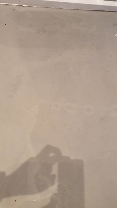 Golv med flytspackel och synliga sprickor i en renoverad hall, skugga av person som fotograferar.