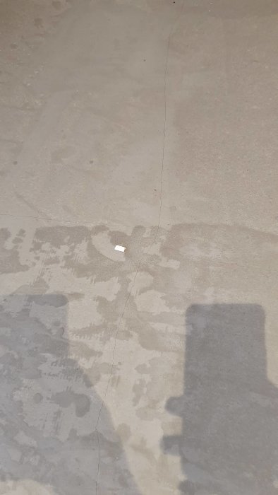 Uppsprickat flytspackel på golv där golvvärme installerats, med synliga skuggor och reflexer.
