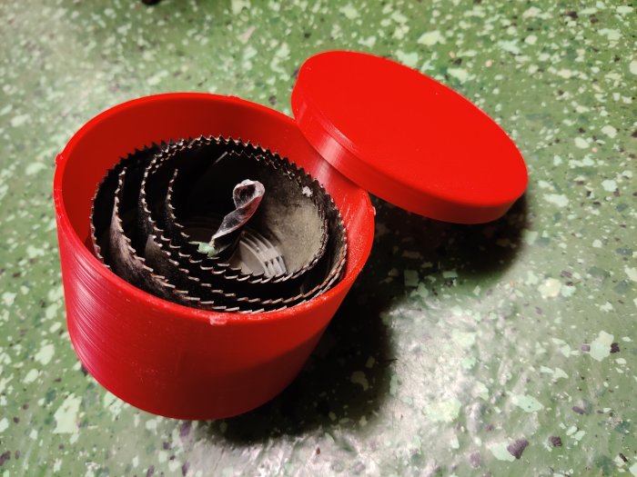 3D-utskrivna röda hålsågsförvaring öppen med åtsittande lock och innehållande sågblad.