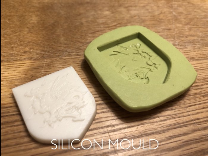 3D-utskriven vaxmodell av sigill och dess silikonform på träbakgrund.
