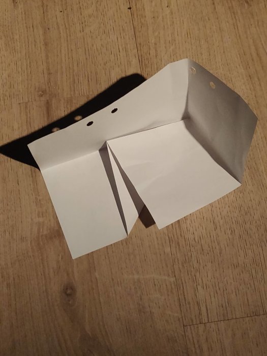 Vitt papper vikt i en specifik form på ett trägolv.