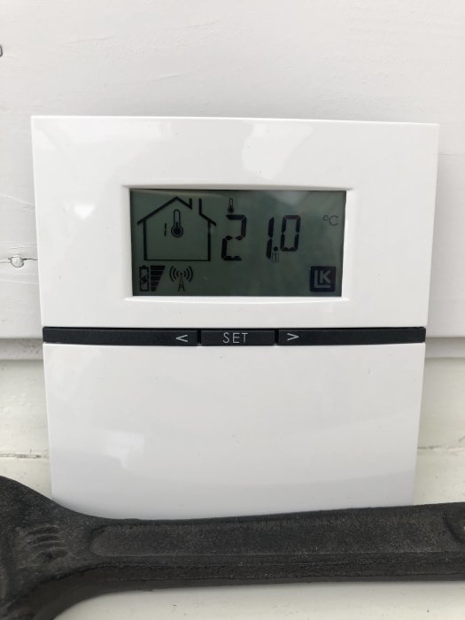 Digital termostat visar 21.0 grader Celsius, monterad på vit vägg, varumärket LK.